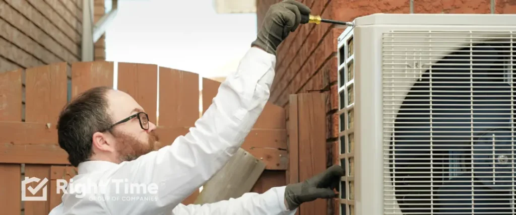 Shines Energy technician inspecting and tightening an outdoor heat pump cabinet in a coastal Halifax side yard to prevent salt-air corrosion before winter.